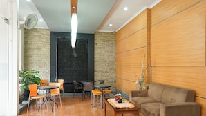A modern lounge area with a wooden wall, a black door, and a seating arrangement including a sofa and tables. - OYO 450 Semampir Residence (Surabaya)