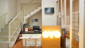 A reception area with a wooden desk, two bar stools, a staircase, and a TV mounted on the wall. - OYO 450 Semampir Residence (Surabaya)