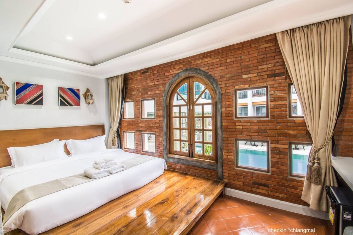A hotel room with a wooden bed, a brick wall, and a large arched window.