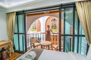 A balcony with a view of brick buildings, a bed, a table, and a chair. - Lanna Oriental Hotel (Chiang Mai)