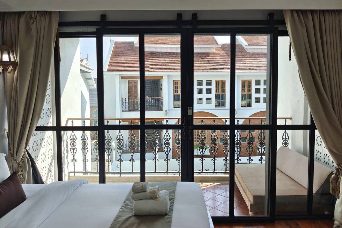 A hotel room with a large bed, a balcony with a view of buildings, and curtains on the windows.
