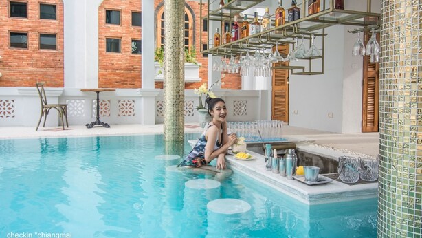 Zona de piscina con un muro de azulejos, una estantería con botellas y vasos, y una silla.