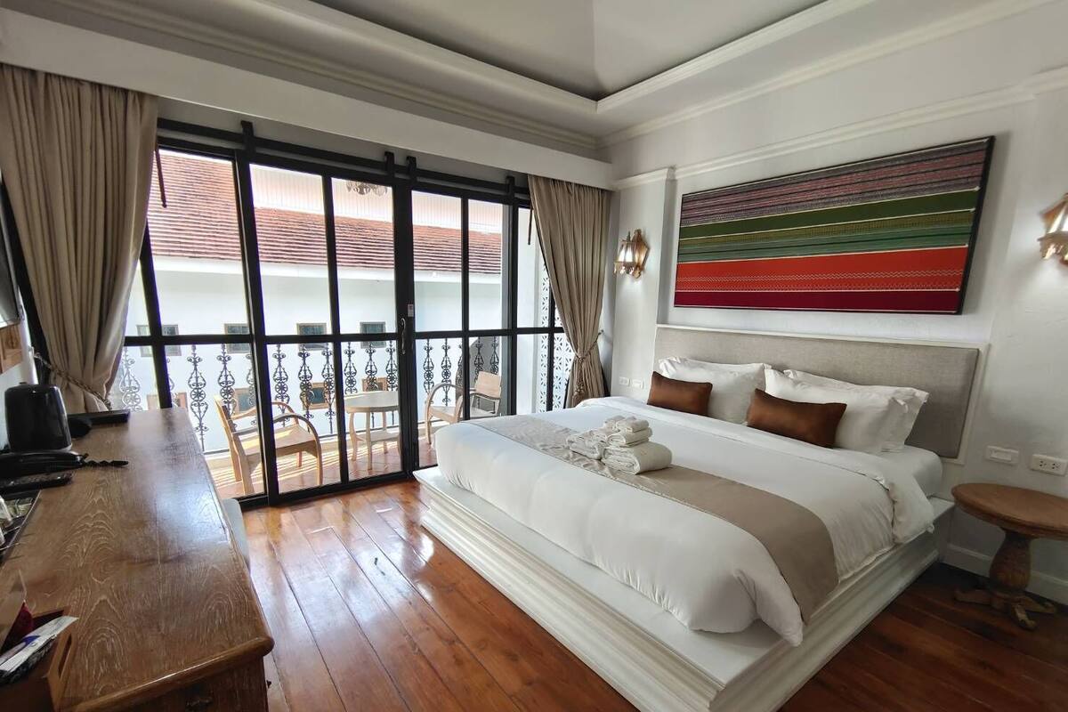 A hotel room with a large bed, a desk, and a balcony with a view.