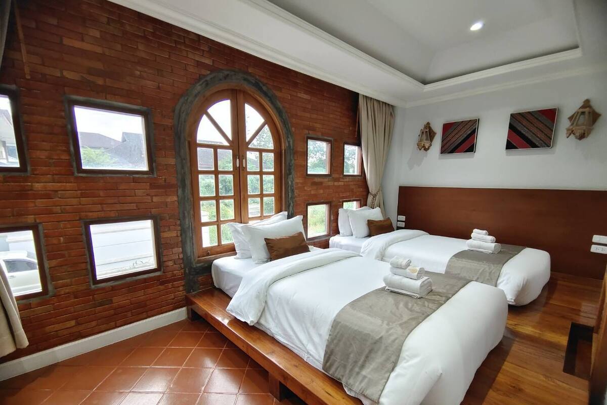 A hotel room with two beds, a brick wall, large windows, and artwork on the walls.