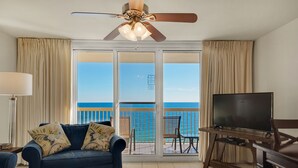 A room with a blue sofa, a television, and a ceiling fan. - Pelican Beach Resort, Directly on the Beach w/breathtaking View (DESTIN)