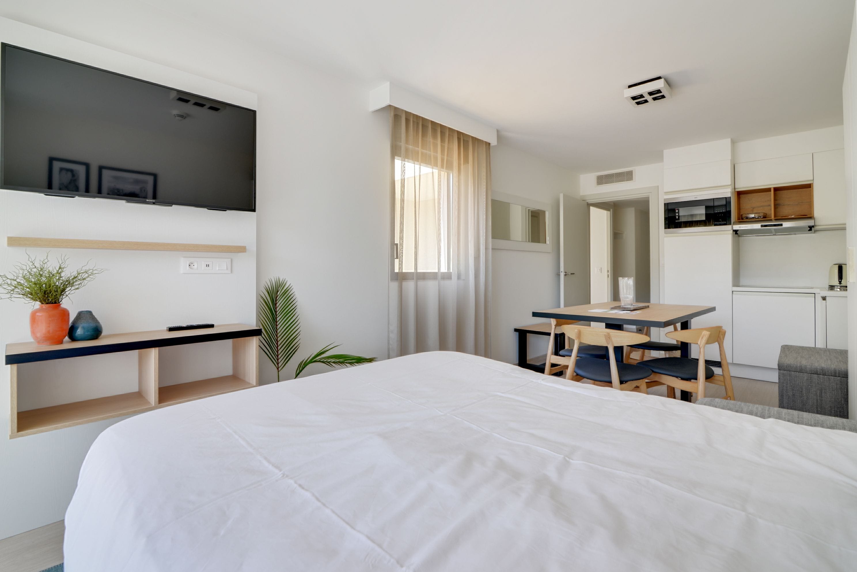 Une chambre d’hôtel moderne dotée d’un grand lit, d’un bureau, d’une chaise, d’un téléviseur fixé au mur et d’un coin cuisine.