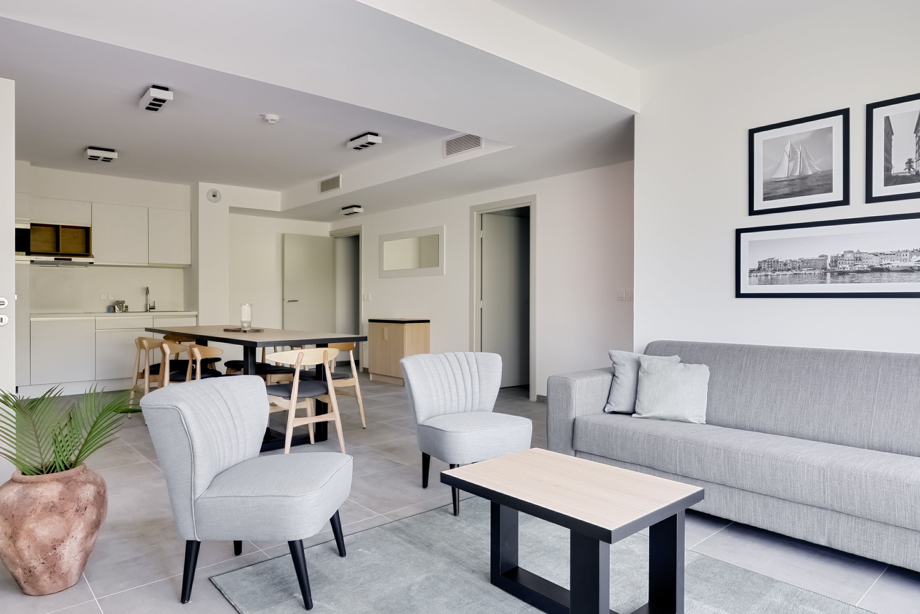 A modern living room with a grey sofa, two armchairs, a coffee table, and a dining area with a table and chairs.