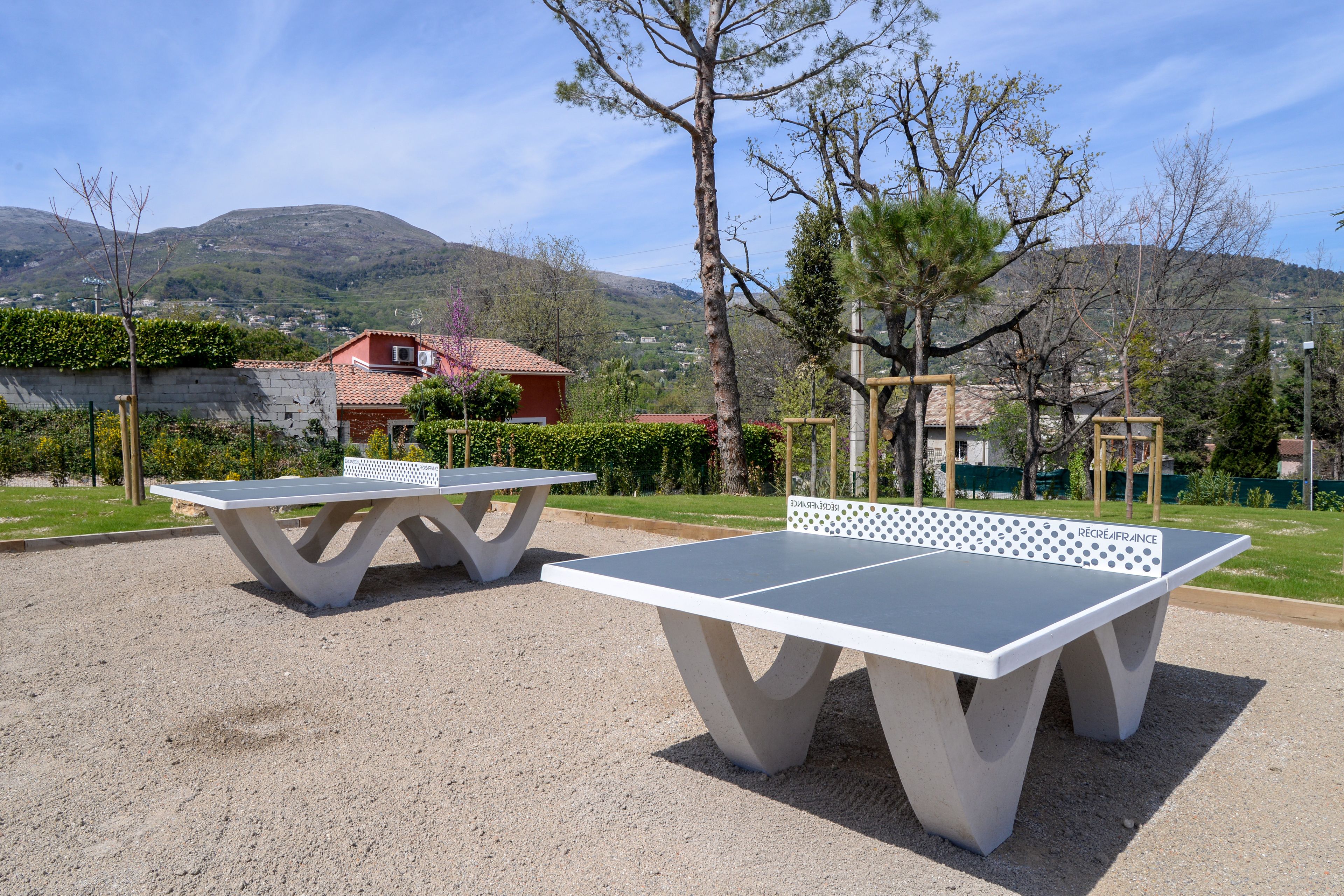 Two outdoor ping pong tables in a park with a mountainous backdrop.