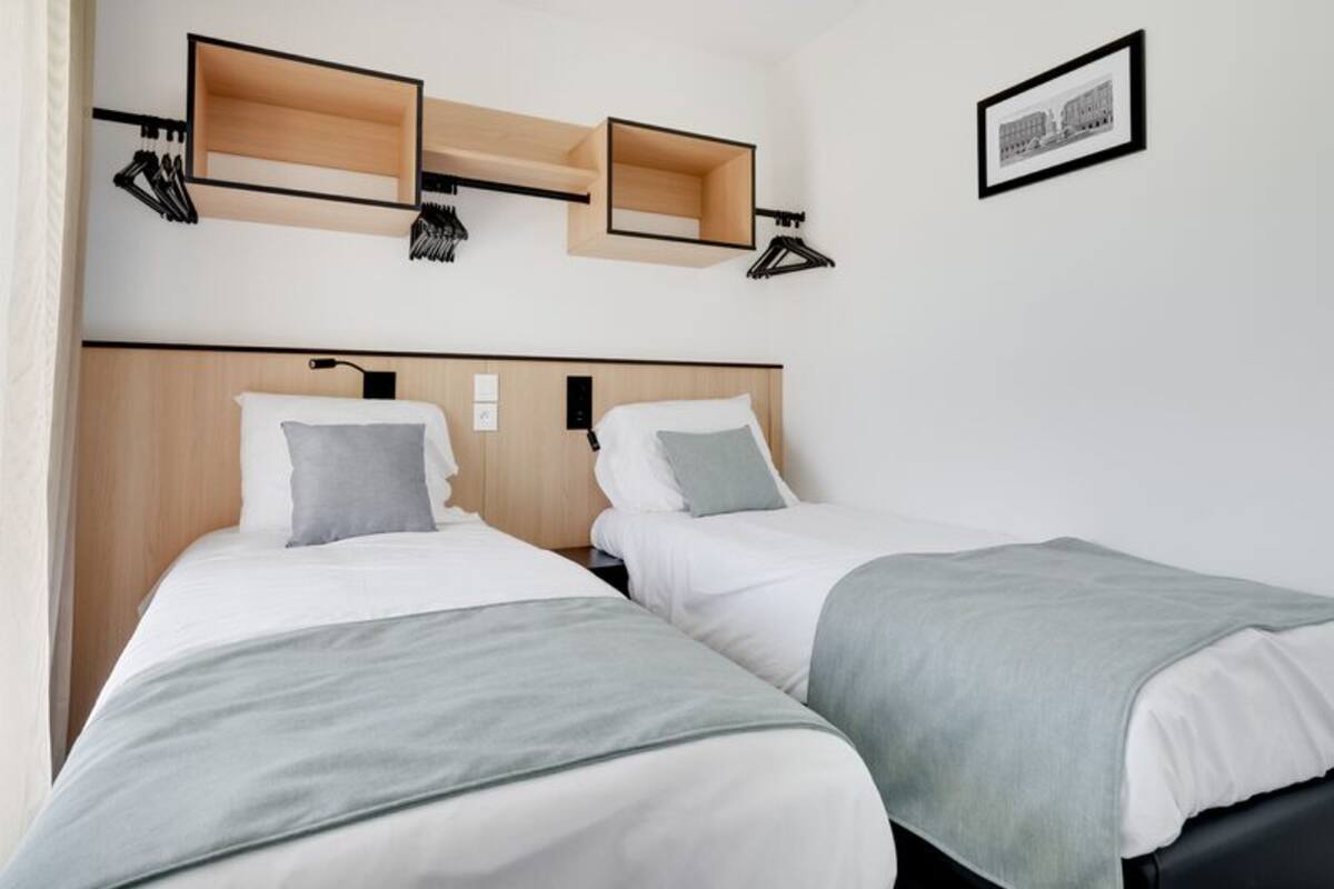 A hotel room with two beds, wooden headboards, and wall-mounted shelves with hanging items.