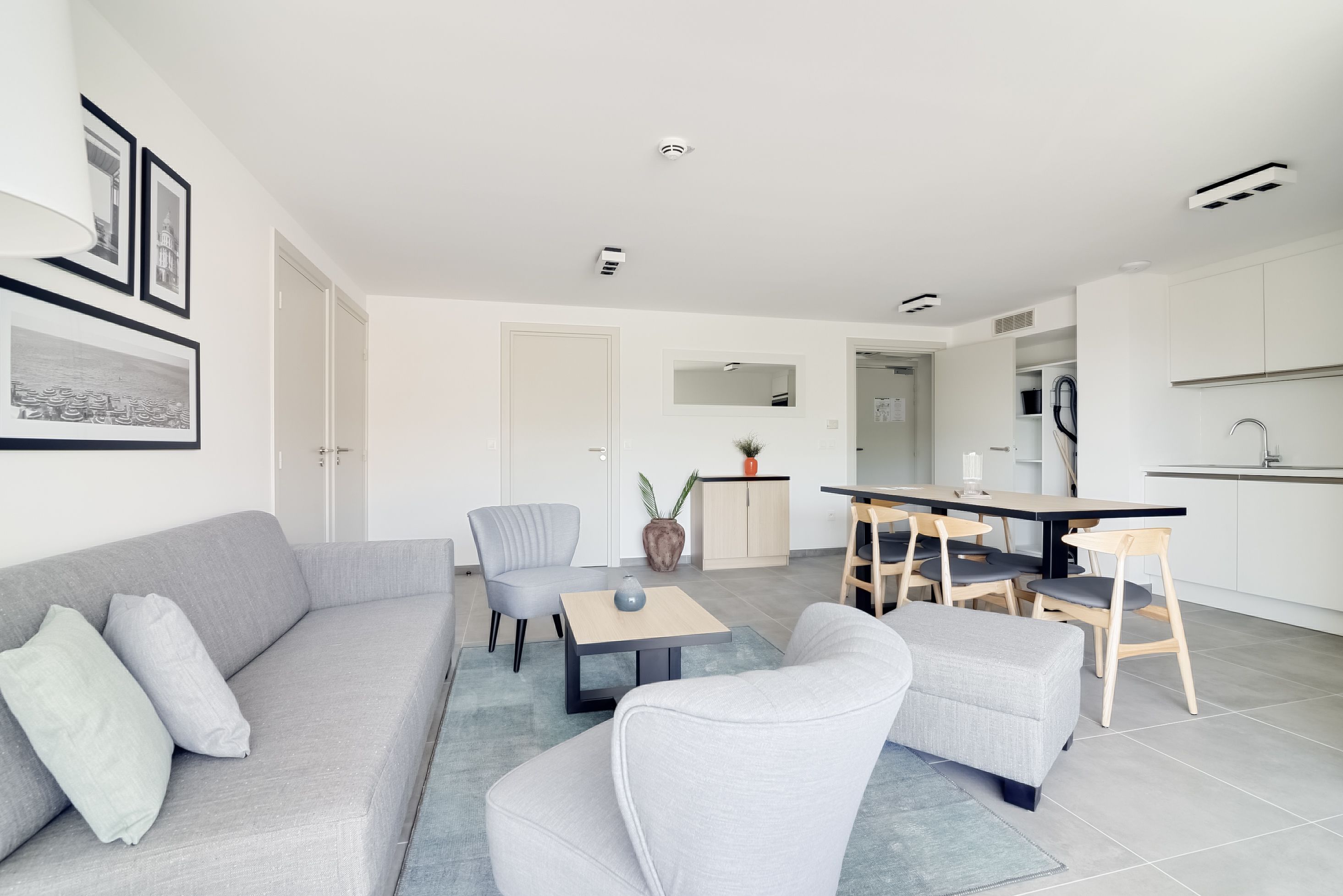 A modern living room with a grey sofa, a coffee table, and a dining area with chairs and a table.