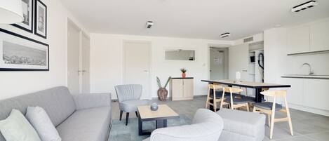 A modern living room with a grey sofa, a coffee table, and a dining area with chairs and a table.