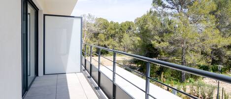 A balcony with a metal railing overlooking a natural landscape with trees and shrubs.