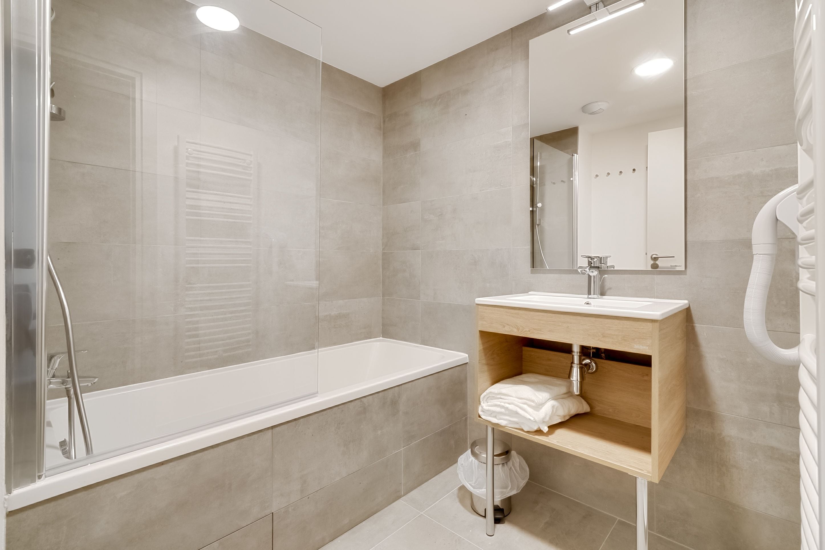 A modern bathroom with a glass-enclosed shower, a wooden vanity with a sink, and a large mirror.