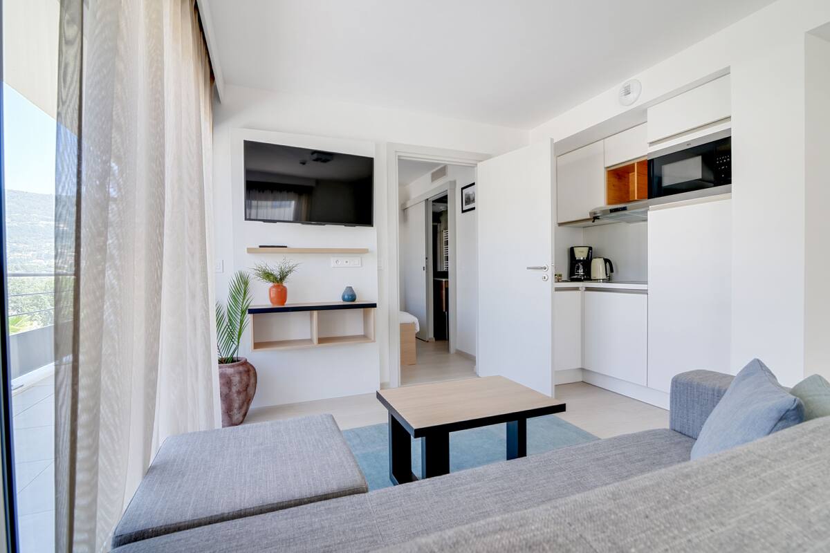 A modern apartment with a living area, kitchenette, and a balcony.