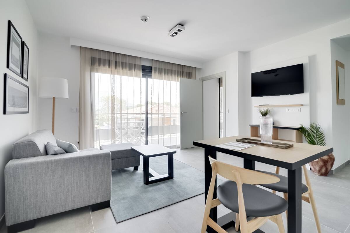 A modern living room with a sofa, a dining table, and a TV mounted on the wall.