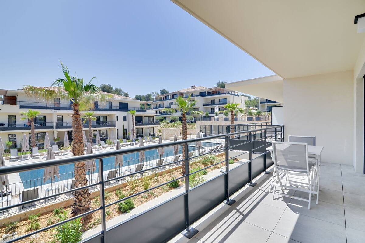 A balcony with a pool view, outdoor seating, and a clear sky.