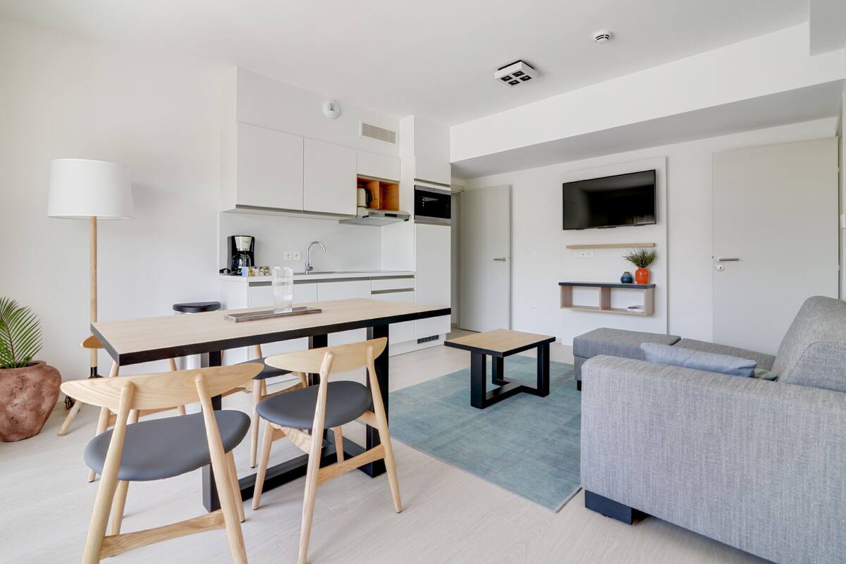 A modern living space with a dining area, kitchen, and a seating area with a sofa and a TV.