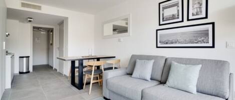A modern living room with a grey sofa, a dining table with chairs, and framed pictures on the wall.
