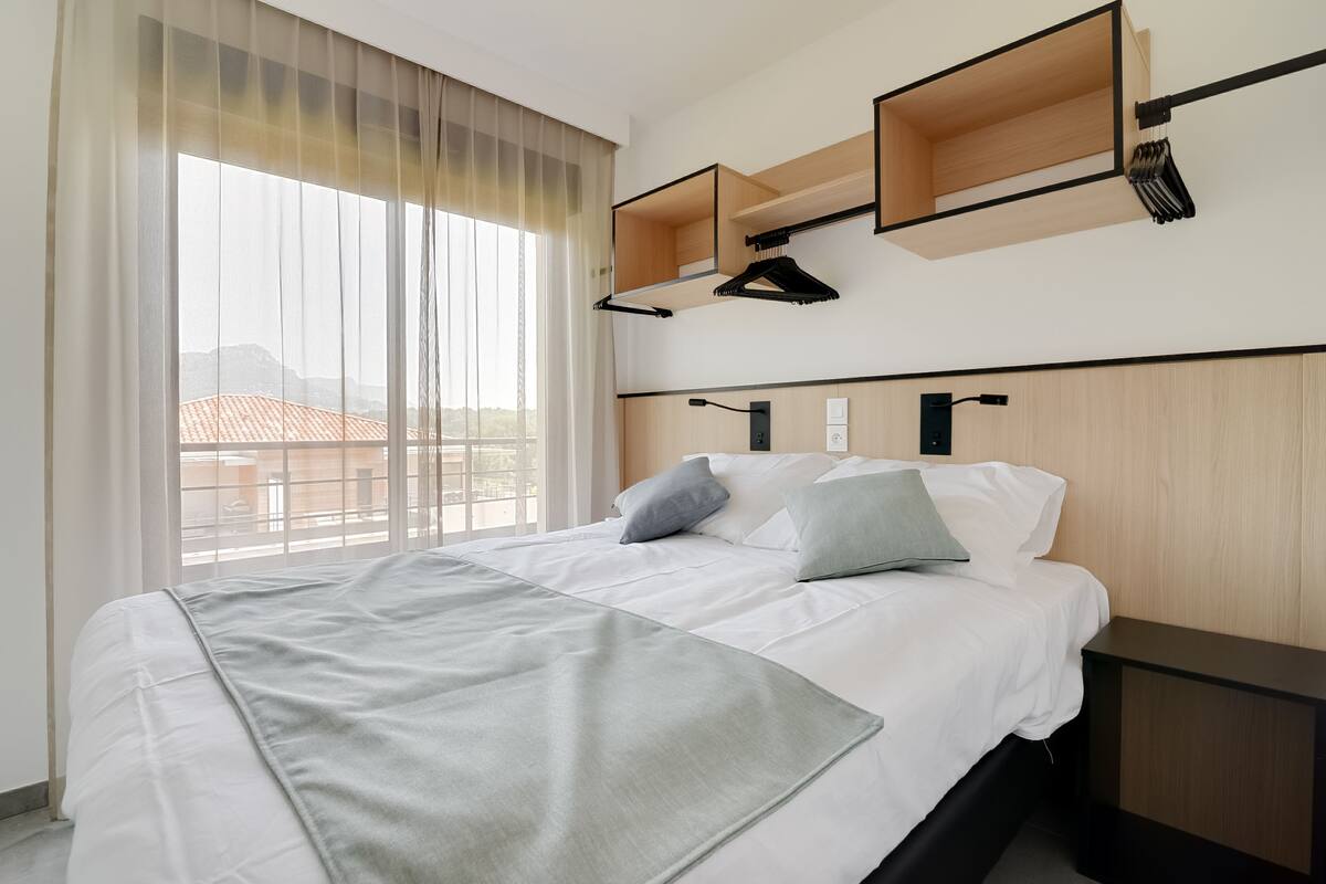 A hotel room with a large bed, a bedside table, a wardrobe, and a window with curtains.