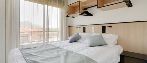 Une chambre d’hôtel avec un grand lit, une table de chevet, une armoire et une fenêtre avec des rideaux.
