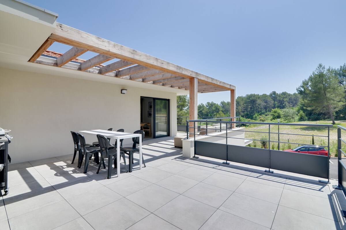 A modern outdoor patio with a dining area, a pergola, and a view of the surrounding landscape.