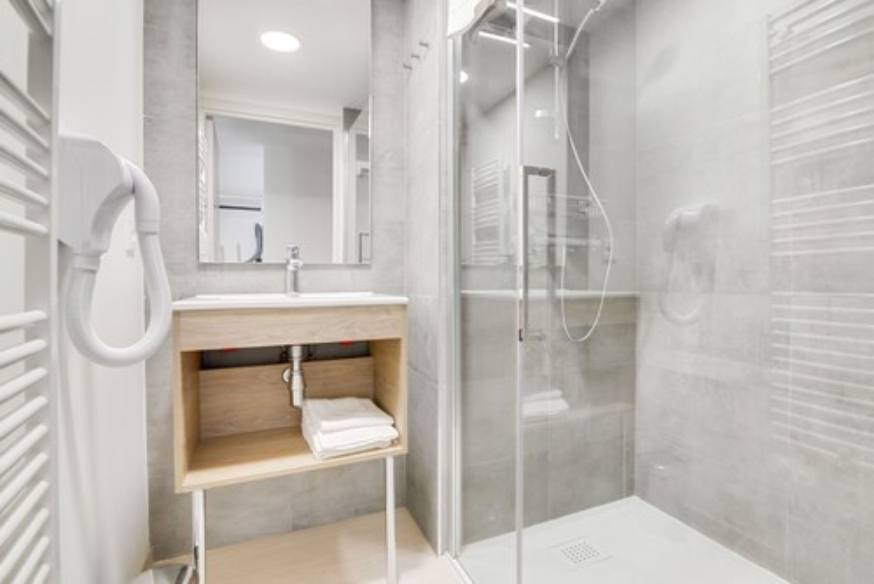 A modern bathroom with a glass-enclosed shower, a white sink, and a mirror above it.