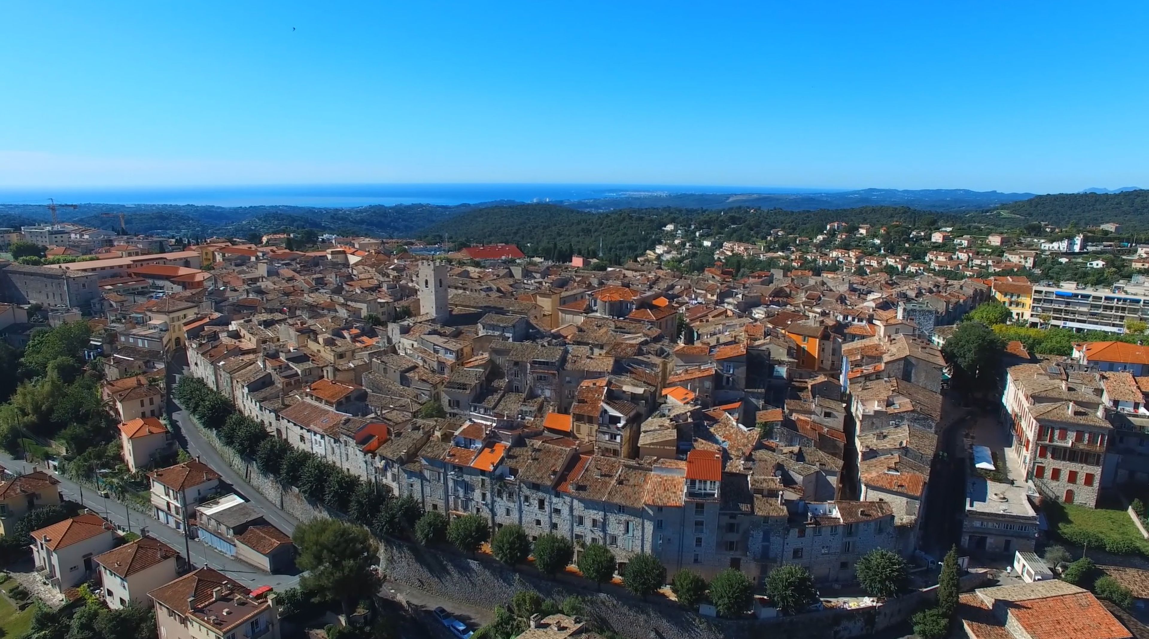 An aerial view of a historic town with dense, closely packed buildings, a prominent stone tower, and a clear view of the surrounding landscape.