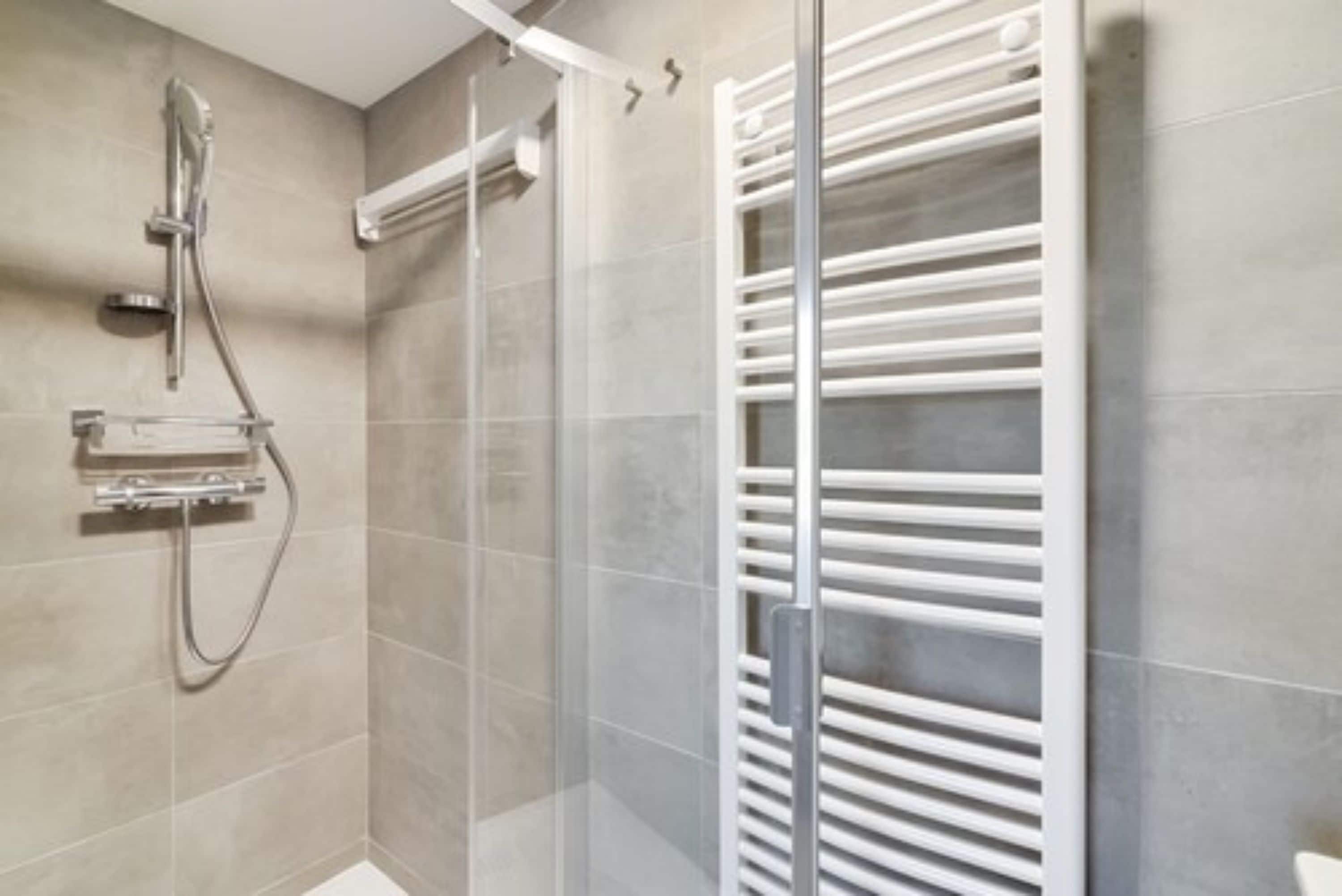 Een moderne badkamer met een glazen douchecabine, een ingebouwde handdoekhouder en een wandradiator.