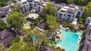 An aerial view of a resort with multiple buildings, a central swimming pool, and surrounding greenery.
