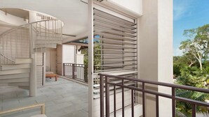 A modern interior with a spiral staircase, a balcony with metal railings, and a view of greenery outside.