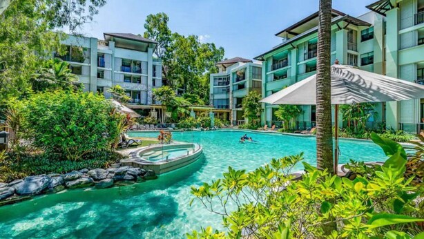 A resort with a central swimming pool surrounded by lush greenery and multi-story buildings.