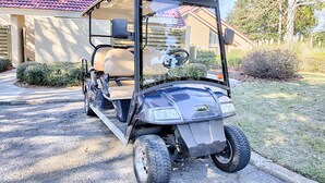 Ein Golfmobil steht vor einem Haus mit rotem Dach und einem Briefkasten mit der Aufschrift 5087.