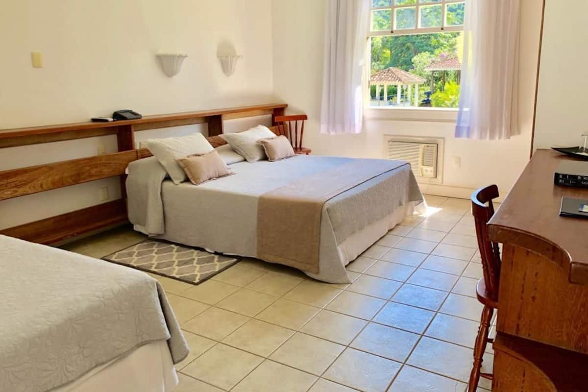 Une chambre avec un grand lit, une table de chevet, une chaise, un bureau et une fenêtre donnant sur un paysage verdoyant.