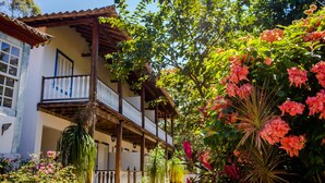 Un edificio de dos plantas con un balcón y un jardín con diversas plantas y flores.