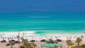 Ein Strand mit klarem türkisblauem Wasser, Sonnenschirmen und Menschen.