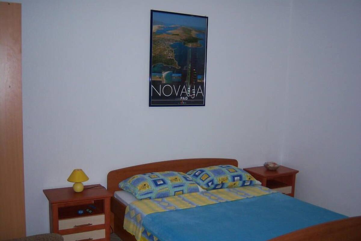 Een slaapkamer met een bed, nachtkastje, lamp en een poster aan de muur.