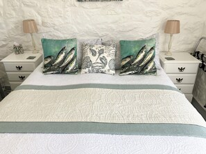 Cama bem arrumada com roupa de cama estampada e dois travesseiros decorativos com desenhos de peixes.