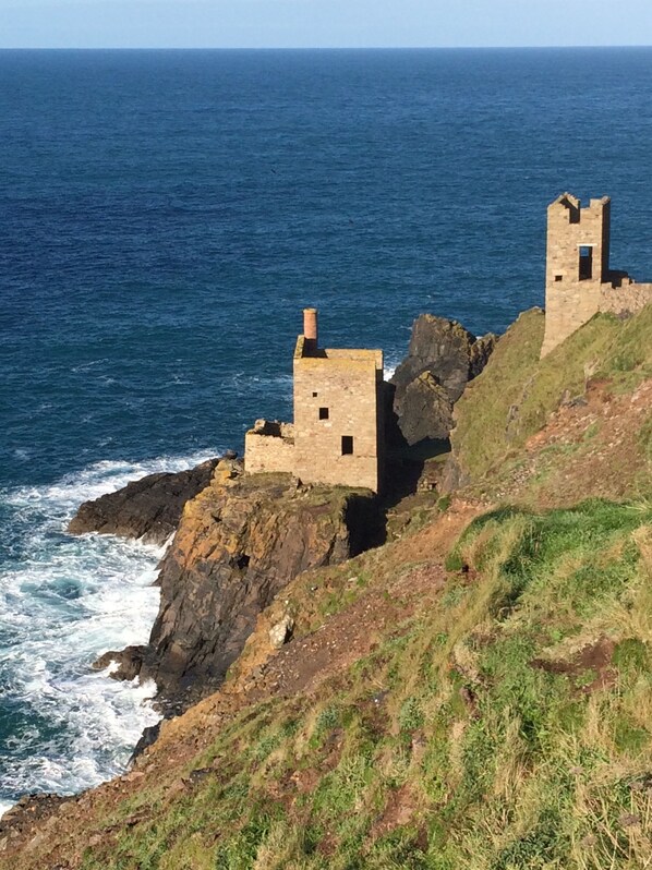 A coastal stone structure with two towers, surrounded by rocky terrain and the ocean. - The Old Post House B&B (Penzance)