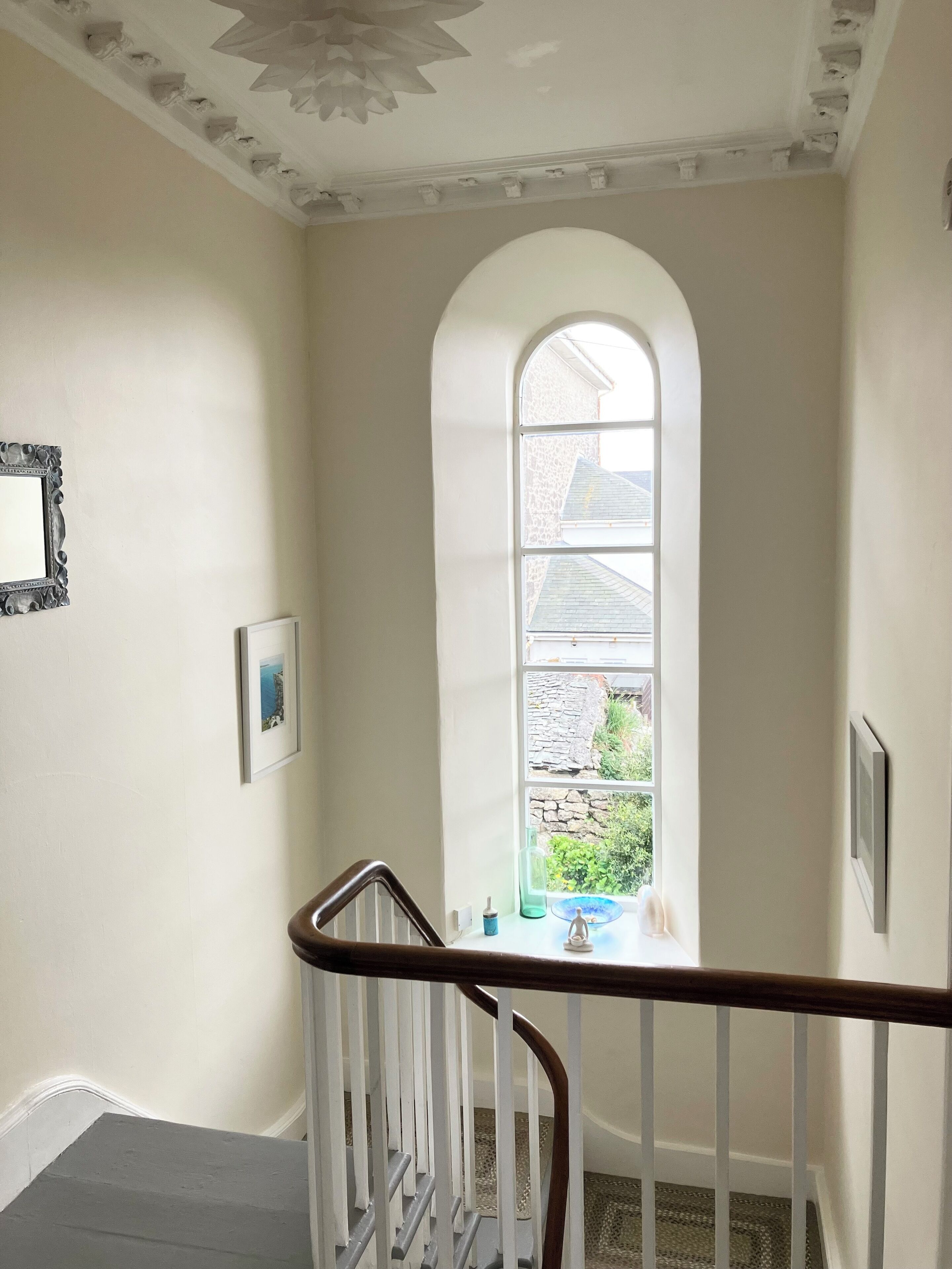 A staircase with a white railing, a large arched window, and a framed picture on the wall.