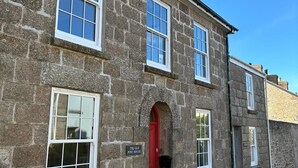 A stone building with a red door, labeled 'The Old Post House,' featuring multiple windows and potted plants. - The Old Post House B&B (Penzance)
