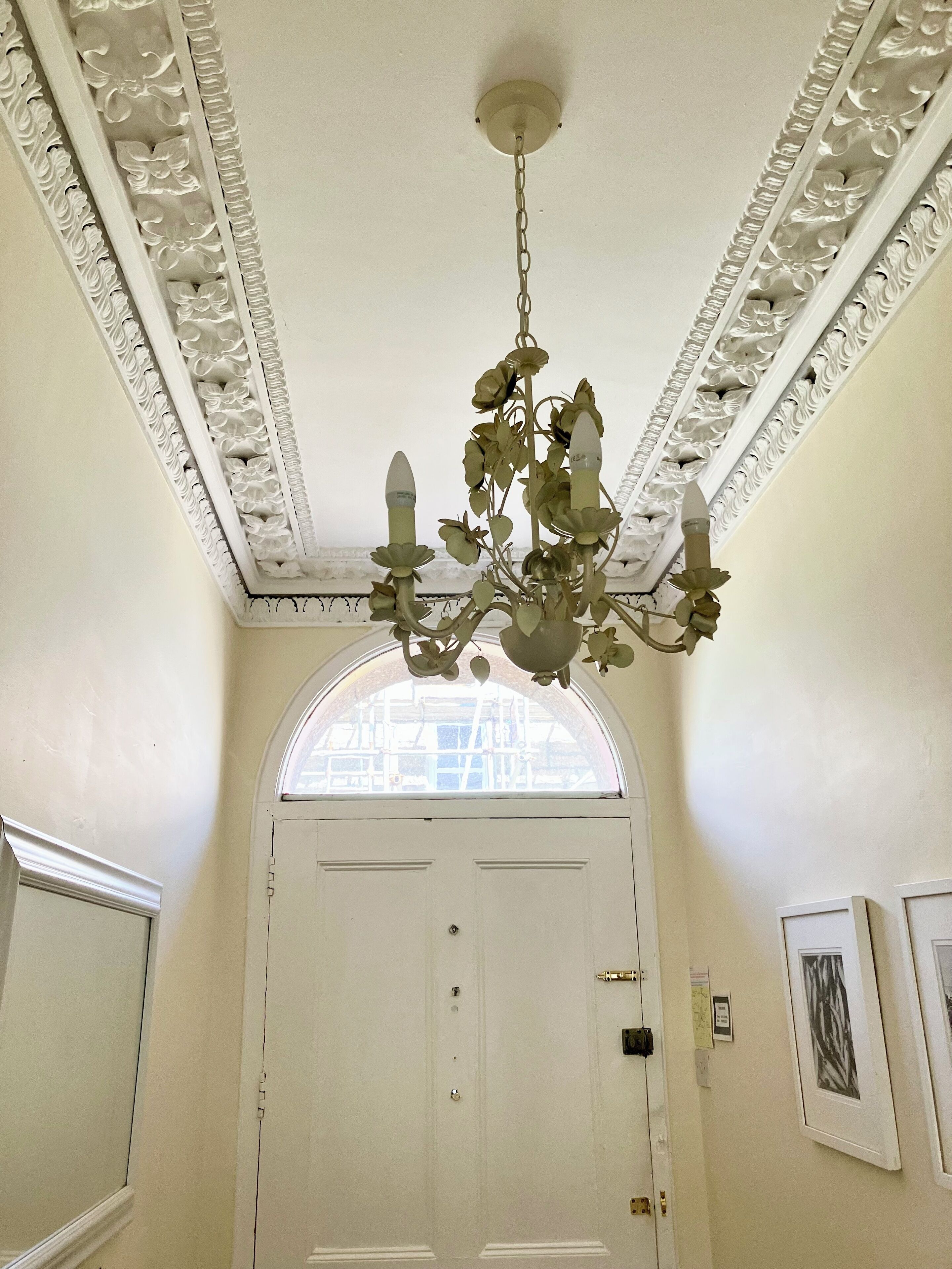 A room with a white door, a chandelier with multiple lights, and a decorative ceiling with intricate patterns.