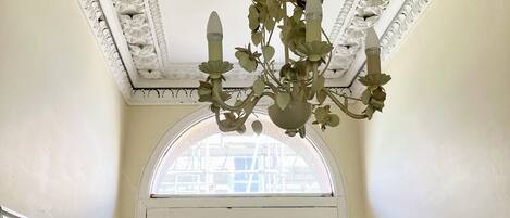 A room with a white door, a chandelier with multiple lights, and a decorative ceiling with intricate patterns.
