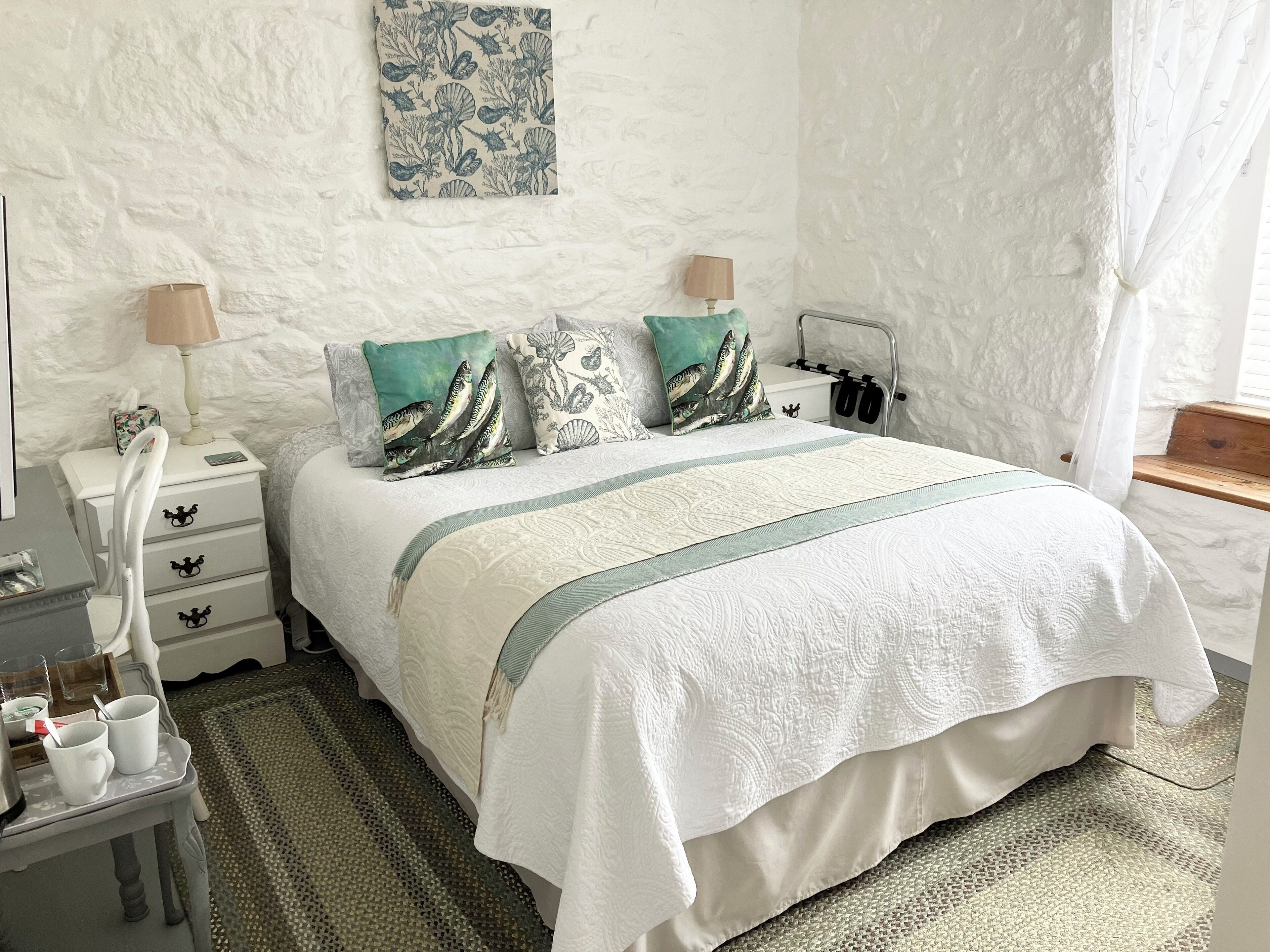 Un dormitorio ordenado con cama, mesitas de noche, lámparas y una obra de arte colgada en la pared.