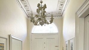 A hallway with a white door, a chandelier, a patterned floor, and a small table with items on it. - The Old Post House B&B (Penzance)