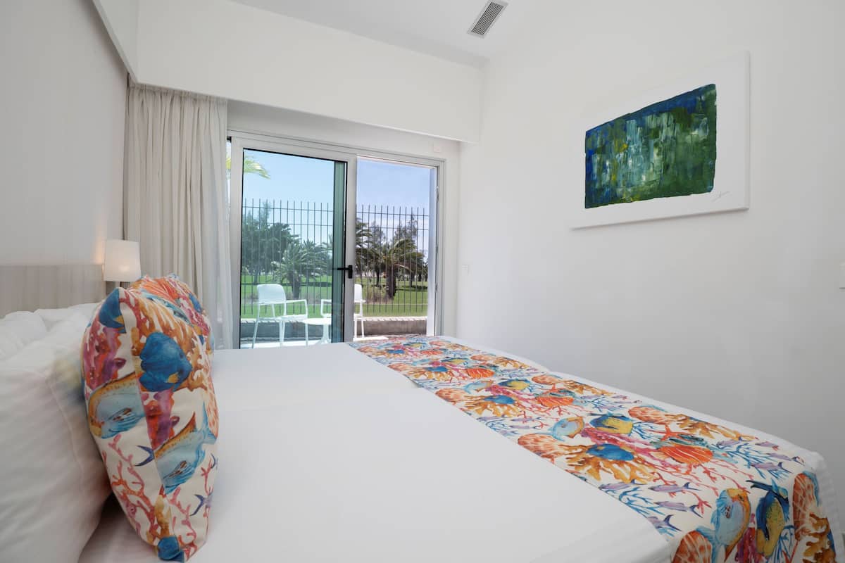 Une chambre d’hôtel avec un lit, un oreiller coloré, un tableau au mur et une vue sur l’extérieur par la fenêtre.