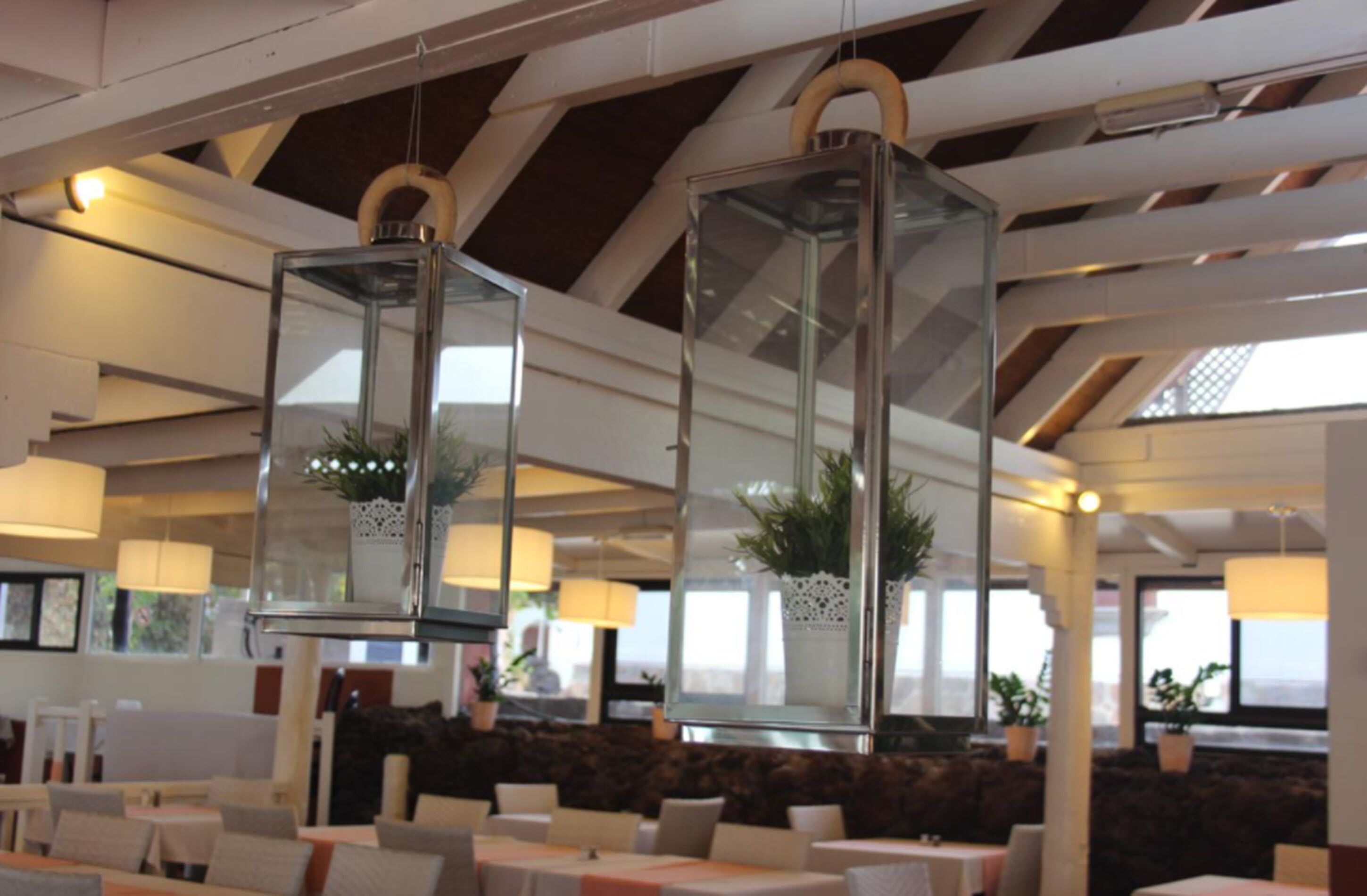 Interior de restaurante con techos altos, faroles de vidrio colgantes con plantas y vista al exterior.