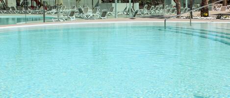 A clear swimming pool with lounge chairs and umbrellas.