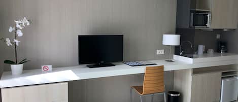 Una cocina moderna con televisor de pantalla plana, encimera blanca, silla de madera, microondas y cafetera.