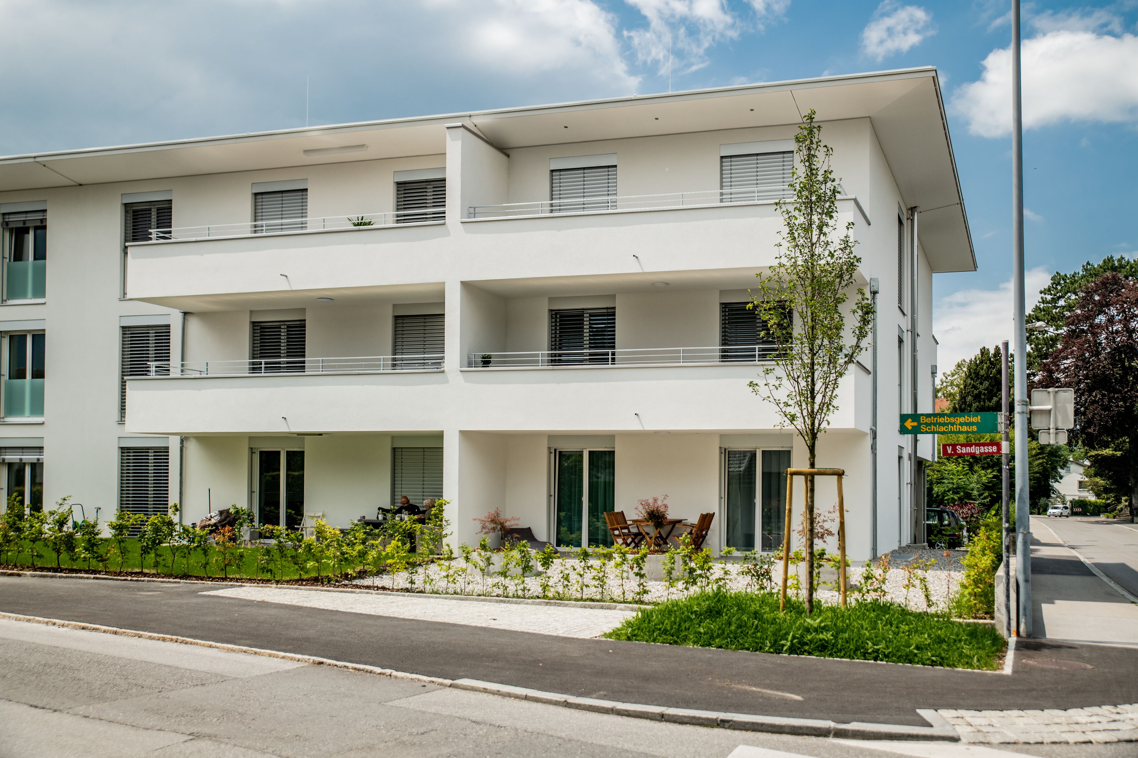 Um edifício moderno de vários andares com varandas, um jardim ajardinado e um céu claro.