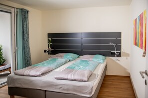 A bedroom with a bed, a headboard, a bedside table, a potted plant, and a colorful artwork on the wall. - City Appartements Dornbirn (Dornbirn)